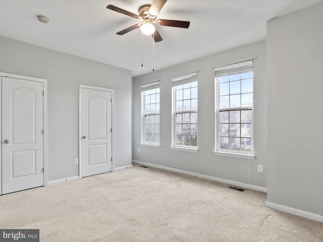 unfurnished bedroom with multiple windows, ceiling fan, and light carpet