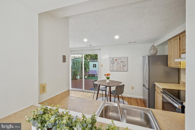 kitchen with stainless steel fridge, stove, a textured ceiling, exhaust hood, and light wood-type flooring