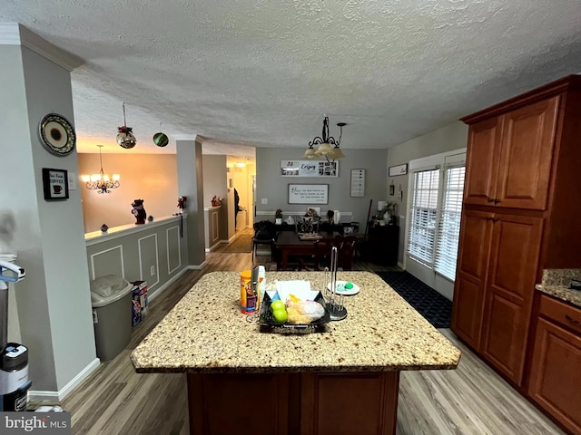 kitchen featuring a center island, light stone countertops, a chandelier, light wood-style flooring, and a textured ceiling