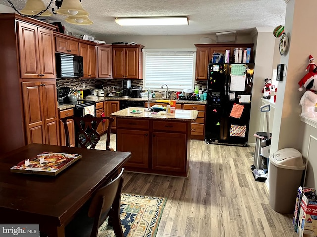 kitchen featuring light stone countertops, light hardwood / wood-style flooring, a textured ceiling, a kitchen island, and black appliances