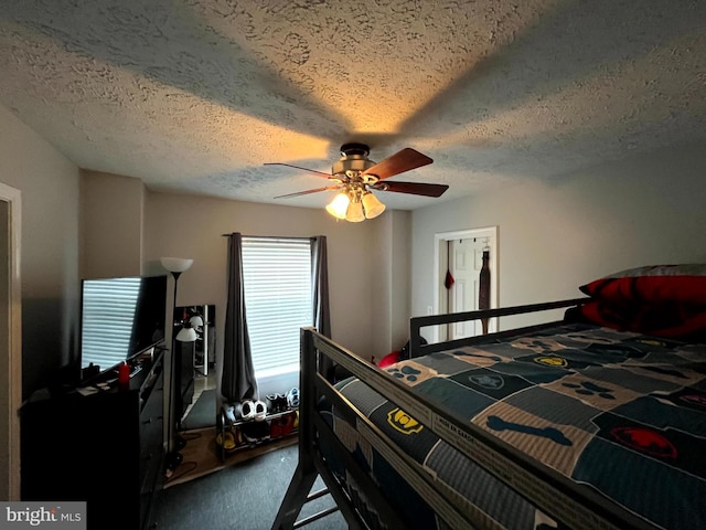 bedroom with a textured ceiling, ceiling fan, and dark carpet