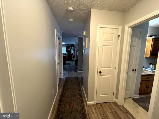 corridor featuring light wood-type flooring and a textured ceiling