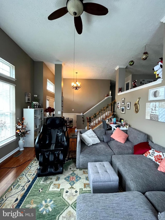 living room featuring stairway, vaulted ceiling, ceiling fan with notable chandelier, wood finished floors, and a textured ceiling