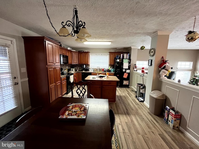 kitchen with a center island, an inviting chandelier, light hardwood / wood-style flooring, decorative light fixtures, and black appliances