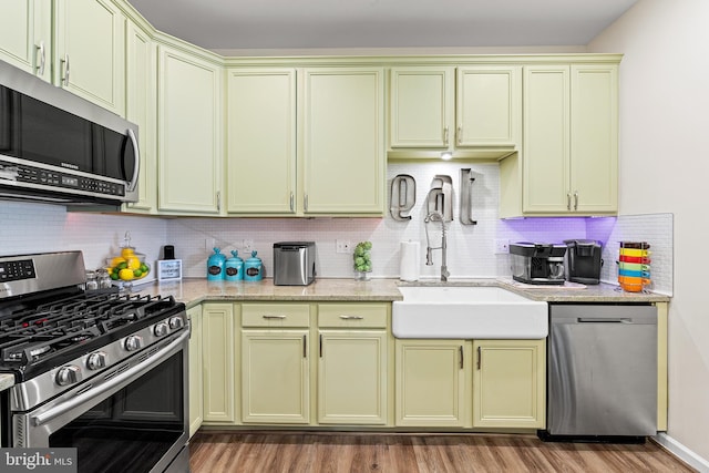 kitchen featuring sink, hardwood / wood-style flooring, light stone countertops, tasteful backsplash, and stainless steel appliances