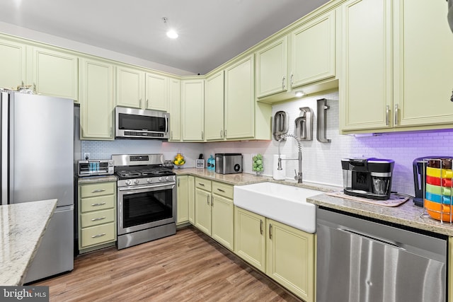 kitchen featuring light stone countertops, sink, tasteful backsplash, appliances with stainless steel finishes, and light wood-type flooring