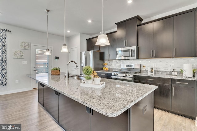 kitchen with a center island with sink, decorative light fixtures, sink, and stainless steel appliances