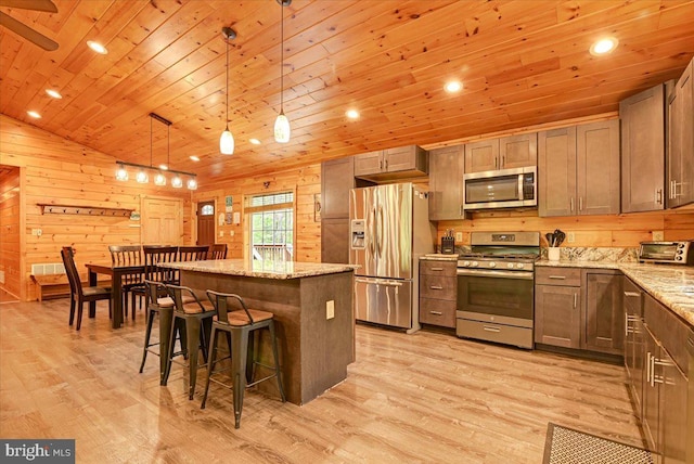 kitchen featuring pendant lighting, light hardwood / wood-style floors, appliances with stainless steel finishes, a kitchen island, and light stone counters