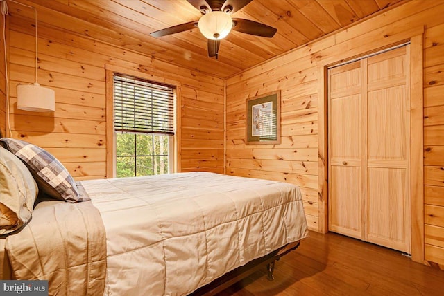 bedroom with ceiling fan, wood walls, wood-type flooring, and wooden ceiling