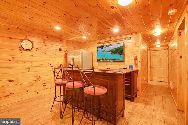 bar featuring wooden ceiling, white refrigerator with ice dispenser, wooden walls, and light hardwood / wood-style flooring