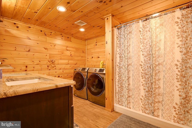 clothes washing area with wood ceiling, wooden walls, sink, washing machine and clothes dryer, and light hardwood / wood-style floors