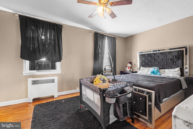 bedroom featuring ceiling fan, cooling unit, radiator heating unit, wood-type flooring, and a textured ceiling