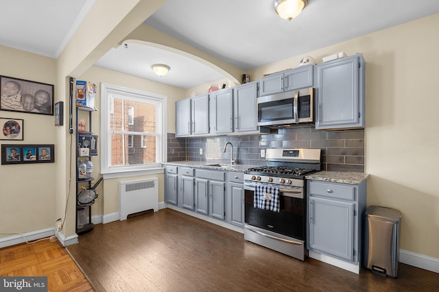 kitchen with stainless steel appliances, gray cabinetry, radiator heating unit, and decorative backsplash