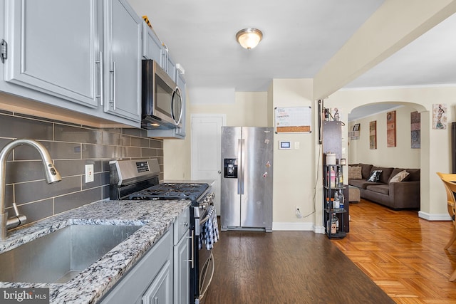 kitchen with sink, appliances with stainless steel finishes, dark parquet floors, light stone countertops, and decorative backsplash