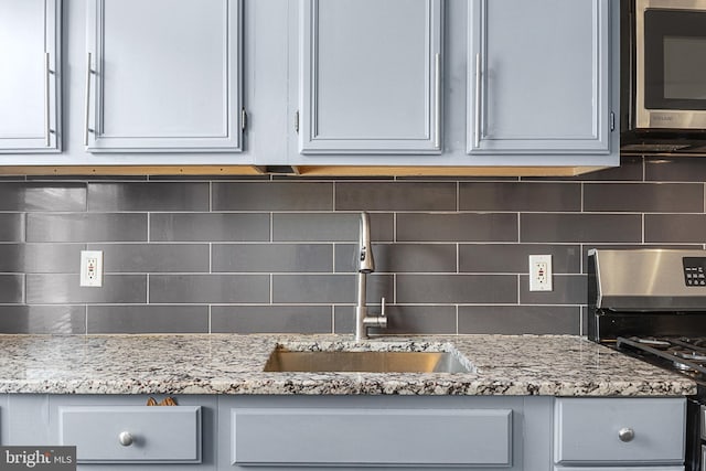 kitchen featuring sink, gray cabinetry, light stone counters, appliances with stainless steel finishes, and decorative backsplash