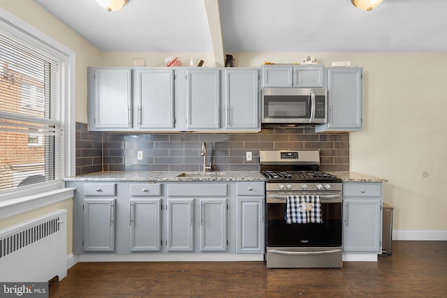 kitchen with appliances with stainless steel finishes, radiator, sink, gray cabinetry, and backsplash