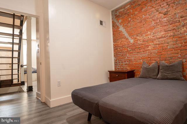 bedroom with hardwood / wood-style floors and brick wall