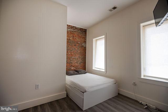 bedroom with dark hardwood / wood-style flooring and brick wall