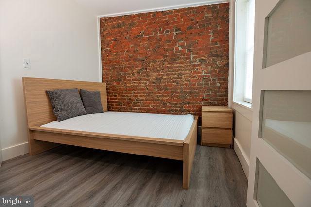 bedroom with dark wood-type flooring and brick wall