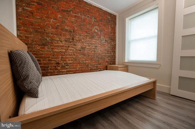 bedroom featuring wood-type flooring, crown molding, and brick wall