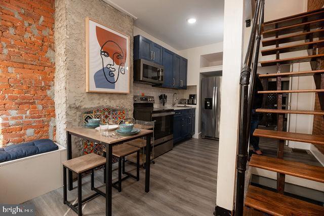 kitchen featuring backsplash, blue cabinets, hardwood / wood-style flooring, appliances with stainless steel finishes, and brick wall