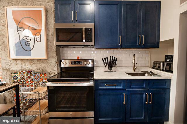 kitchen featuring blue cabinetry, backsplash, sink, and stainless steel appliances