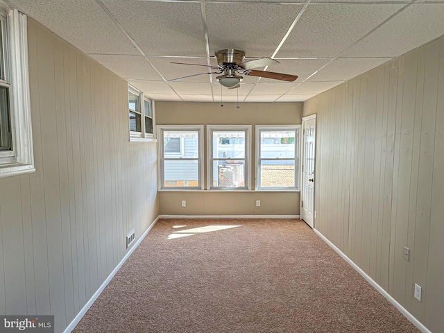 spare room with a drop ceiling, ceiling fan, carpet floors, and wooden walls