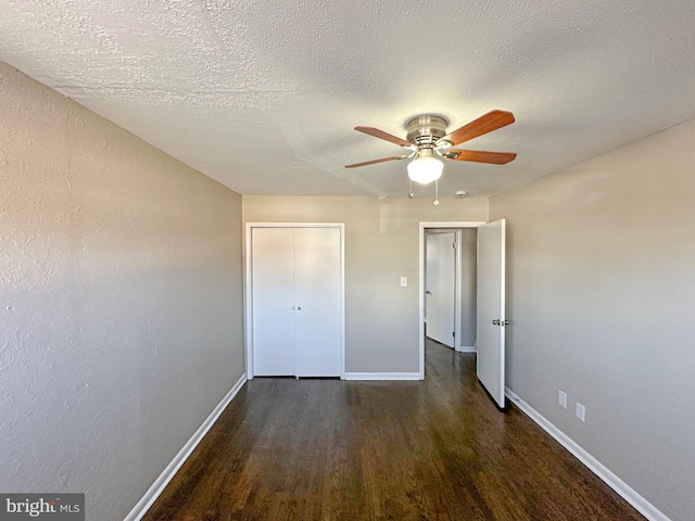 unfurnished bedroom with a textured ceiling, ceiling fan, dark wood-type flooring, and a closet