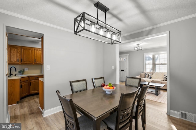 dining space with a textured ceiling, light wood-type flooring, ornamental molding, and sink