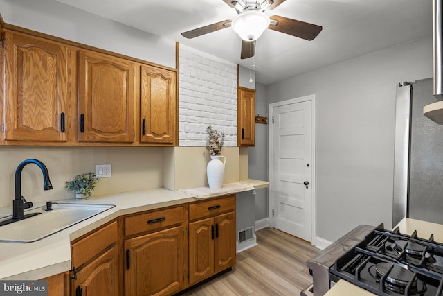 kitchen with ceiling fan, sink, range with gas cooktop, and light wood-type flooring