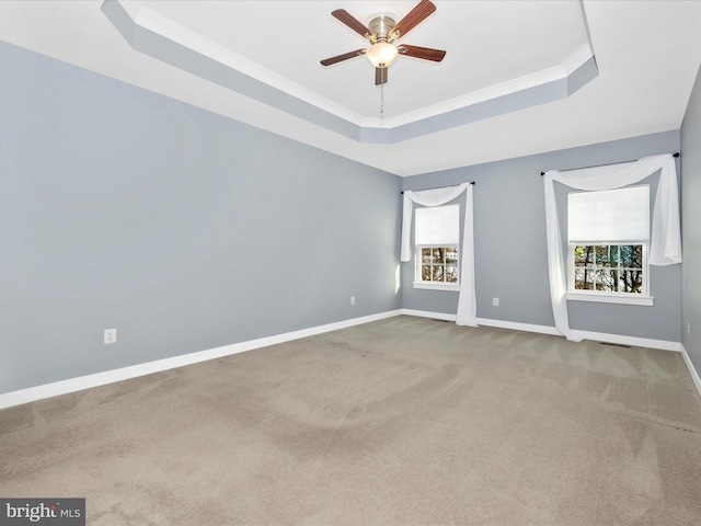 carpeted empty room with ceiling fan, a wealth of natural light, and a tray ceiling