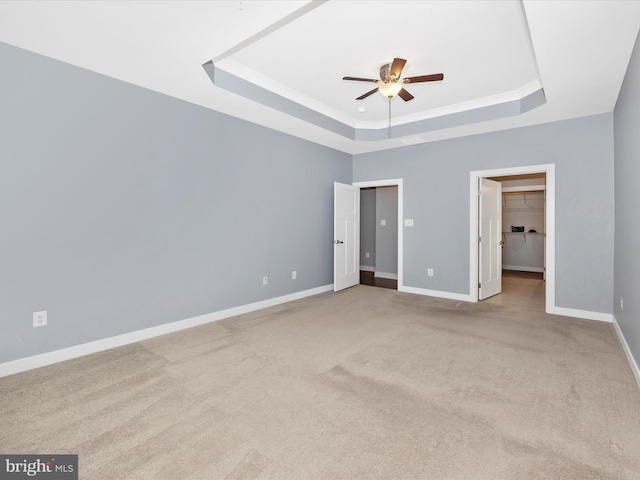 unfurnished bedroom with a spacious closet, ceiling fan, a tray ceiling, light carpet, and a closet