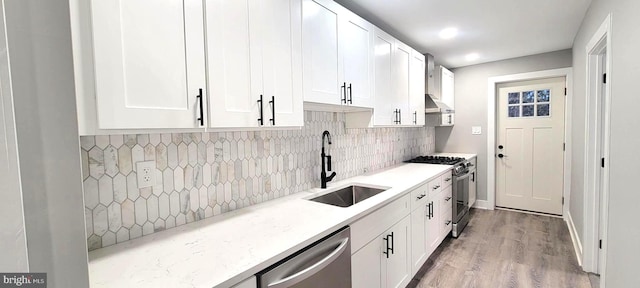 kitchen featuring sink, range hood, appliances with stainless steel finishes, light hardwood / wood-style floors, and white cabinetry