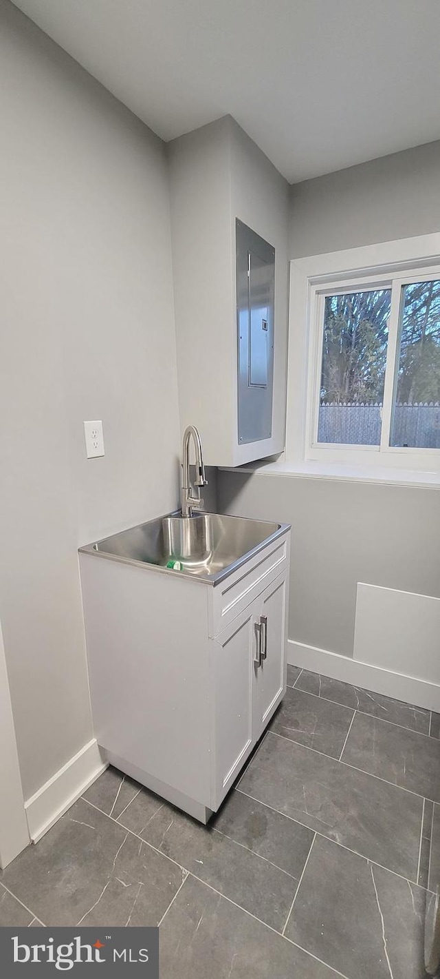 kitchen featuring electric panel, white cabinetry, sink, and stainless steel counters