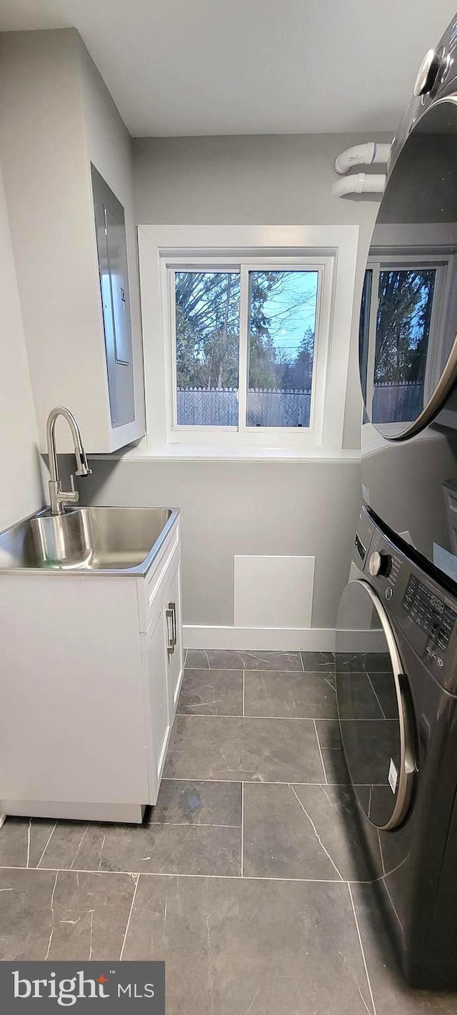 laundry area featuring electric panel, stacked washer and dryer, cabinets, and sink