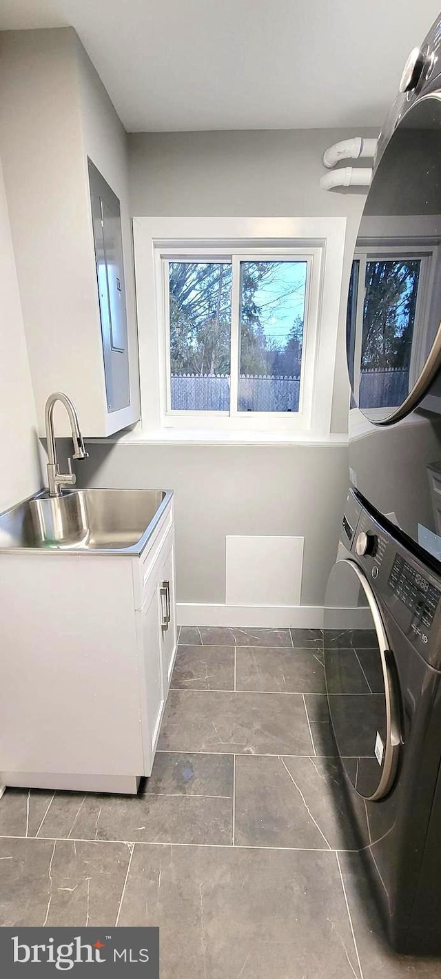 clothes washing area featuring electric panel, sink, cabinets, and stacked washer / drying machine