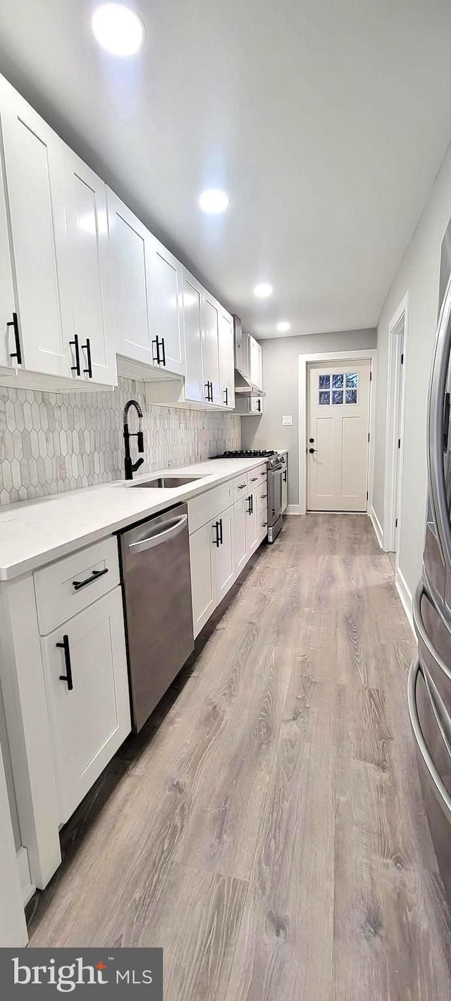 kitchen with white cabinets, sink, decorative backsplash, light wood-type flooring, and stainless steel appliances