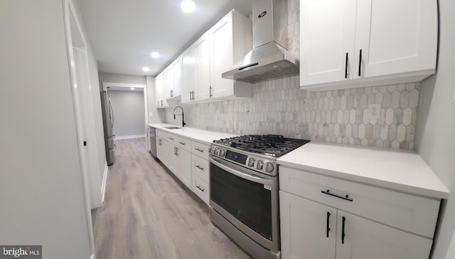 kitchen featuring decorative backsplash, wall chimney exhaust hood, stainless steel appliances, sink, and white cabinetry