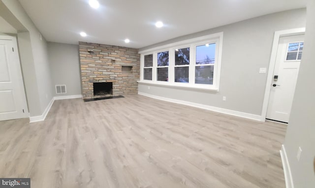 unfurnished living room featuring a stone fireplace and light wood-type flooring