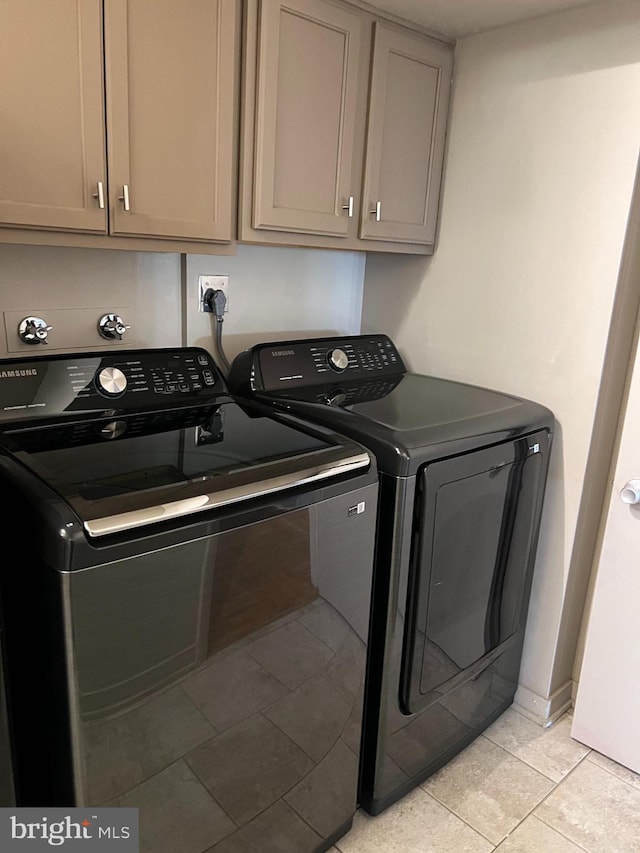 clothes washing area featuring separate washer and dryer, light tile patterned flooring, and cabinets