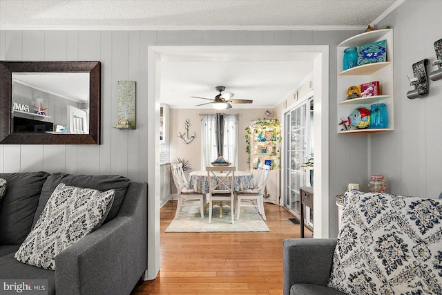 dining area featuring hardwood / wood-style floors, wood walls, crown molding, ceiling fan, and a textured ceiling