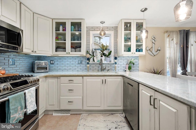 kitchen featuring light stone countertops, white cabinets, pendant lighting, and appliances with stainless steel finishes