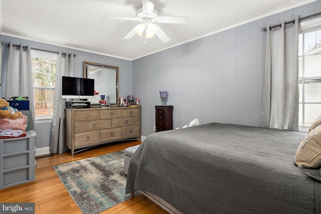 bedroom featuring wooden walls, light hardwood / wood-style flooring, ceiling fan, and ornamental molding