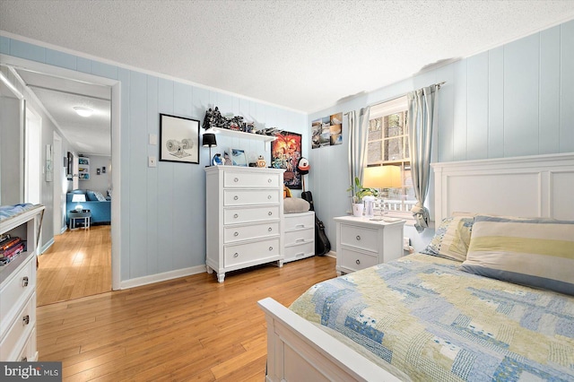 bedroom with light wood-type flooring, a textured ceiling, and ornamental molding