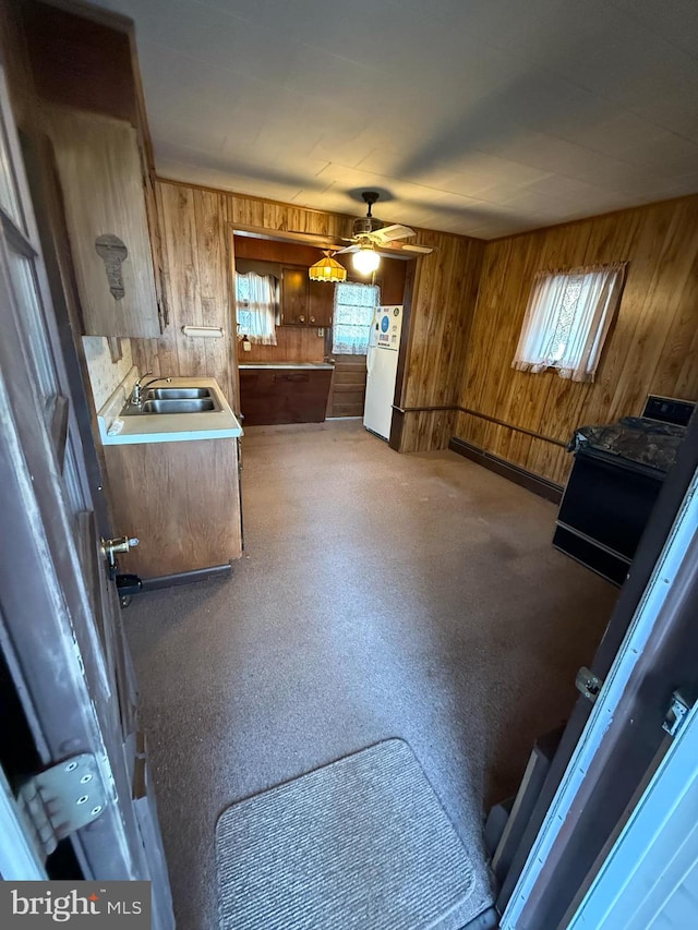 kitchen featuring a wealth of natural light, wooden walls, sink, white fridge, and black range with electric stovetop