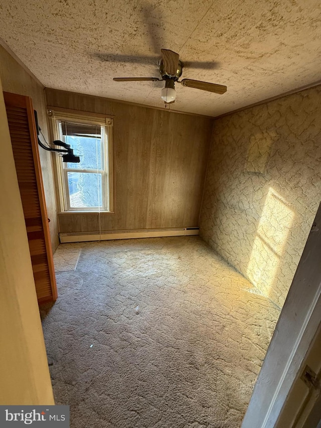 carpeted spare room with ceiling fan, wood walls, and a baseboard heating unit