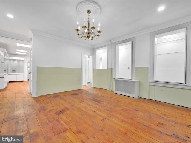 empty room featuring radiator heating unit, an inviting chandelier, light hardwood / wood-style flooring, and ornamental molding