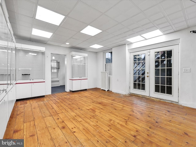 empty room with a paneled ceiling, light wood-type flooring, radiator, and french doors