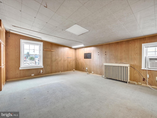 carpeted spare room featuring radiator heating unit, plenty of natural light, and wooden walls