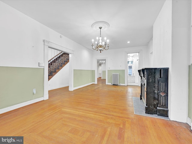 unfurnished living room featuring a notable chandelier, radiator heating unit, and light parquet flooring